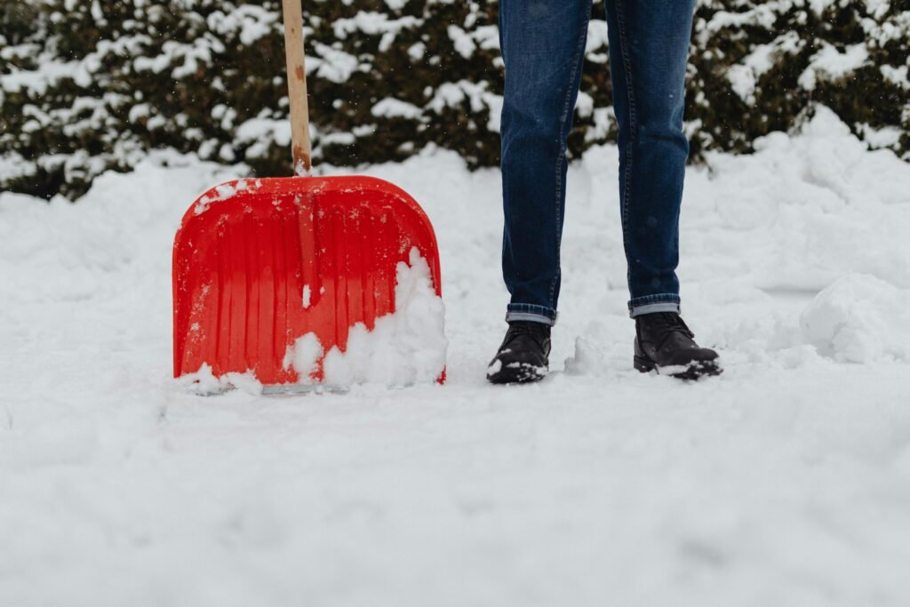 A person shoveling heavy winter snowfall using a red snow shovel. Outdoor winter scene.